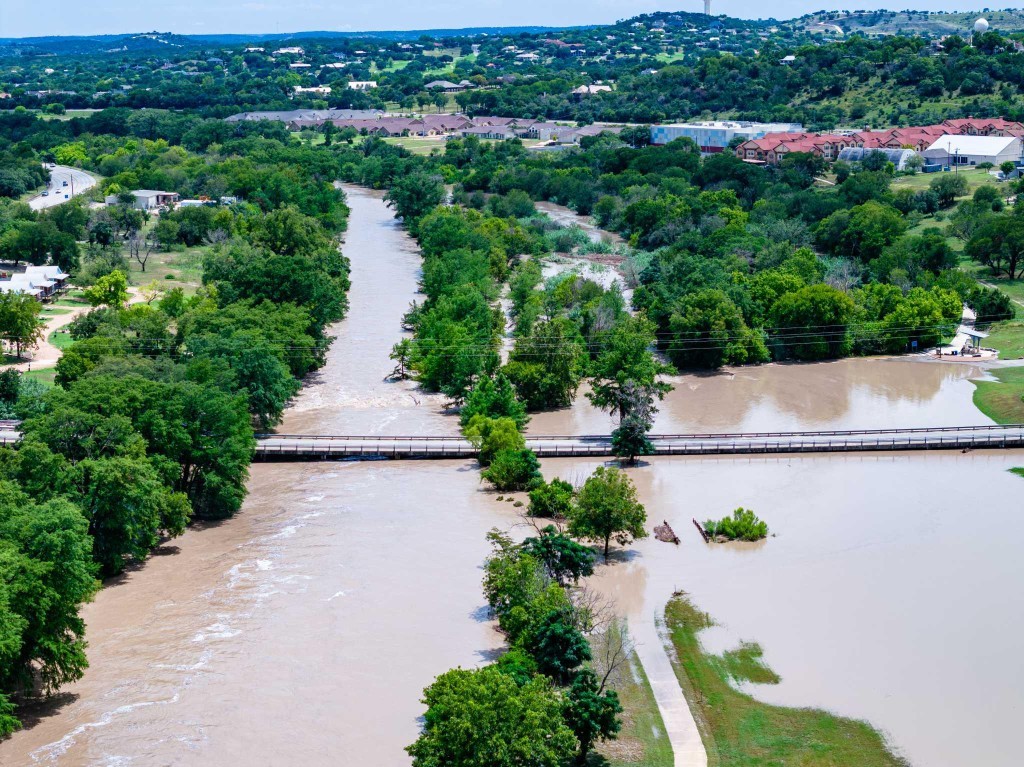 Aerial view of a flooded Texas river corridor with a bridge and nearby community, illustrating flood-risk and infrastructure planning needs